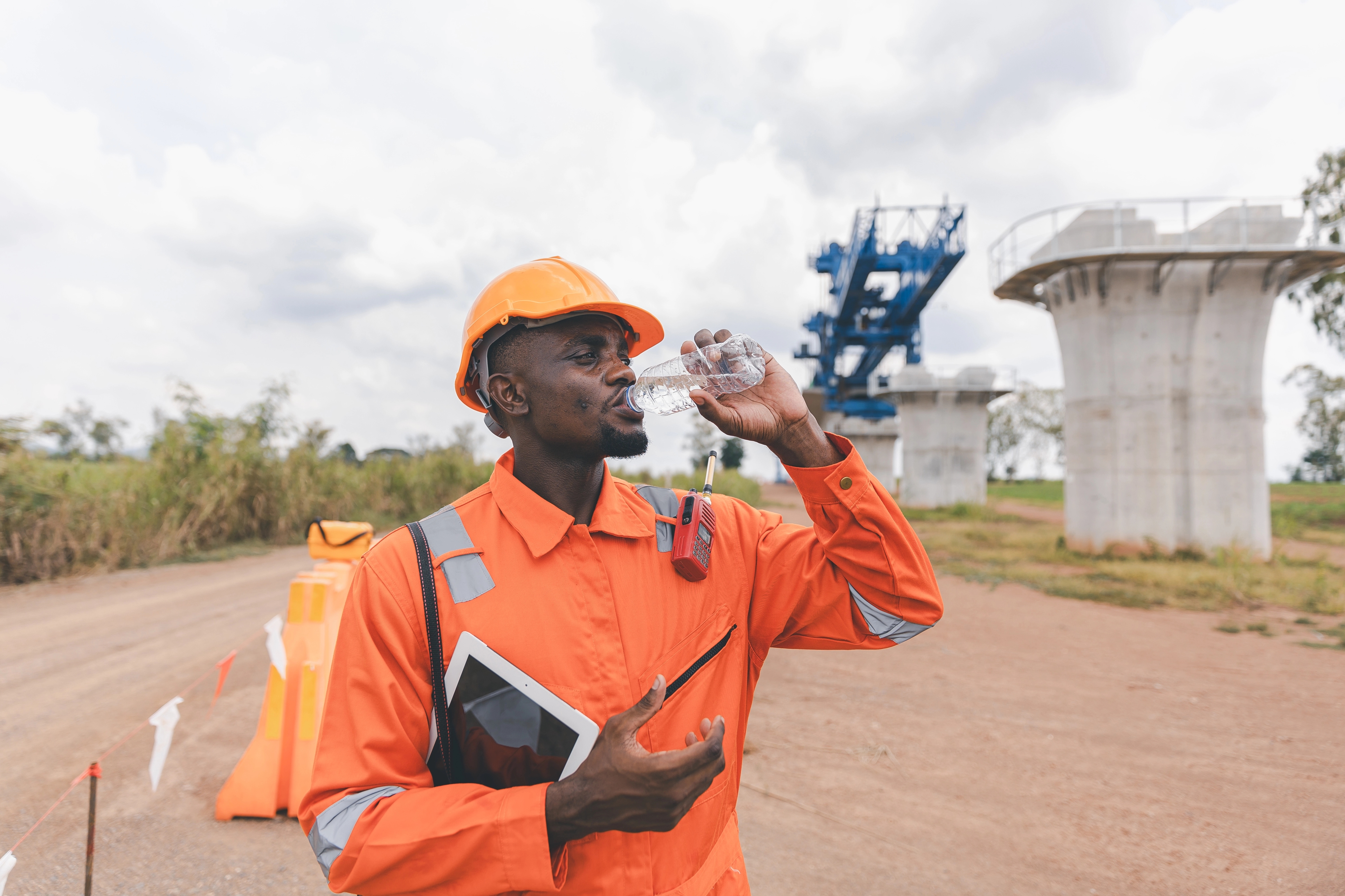 An image of a african miner in orange overalls drinking a bottle of water