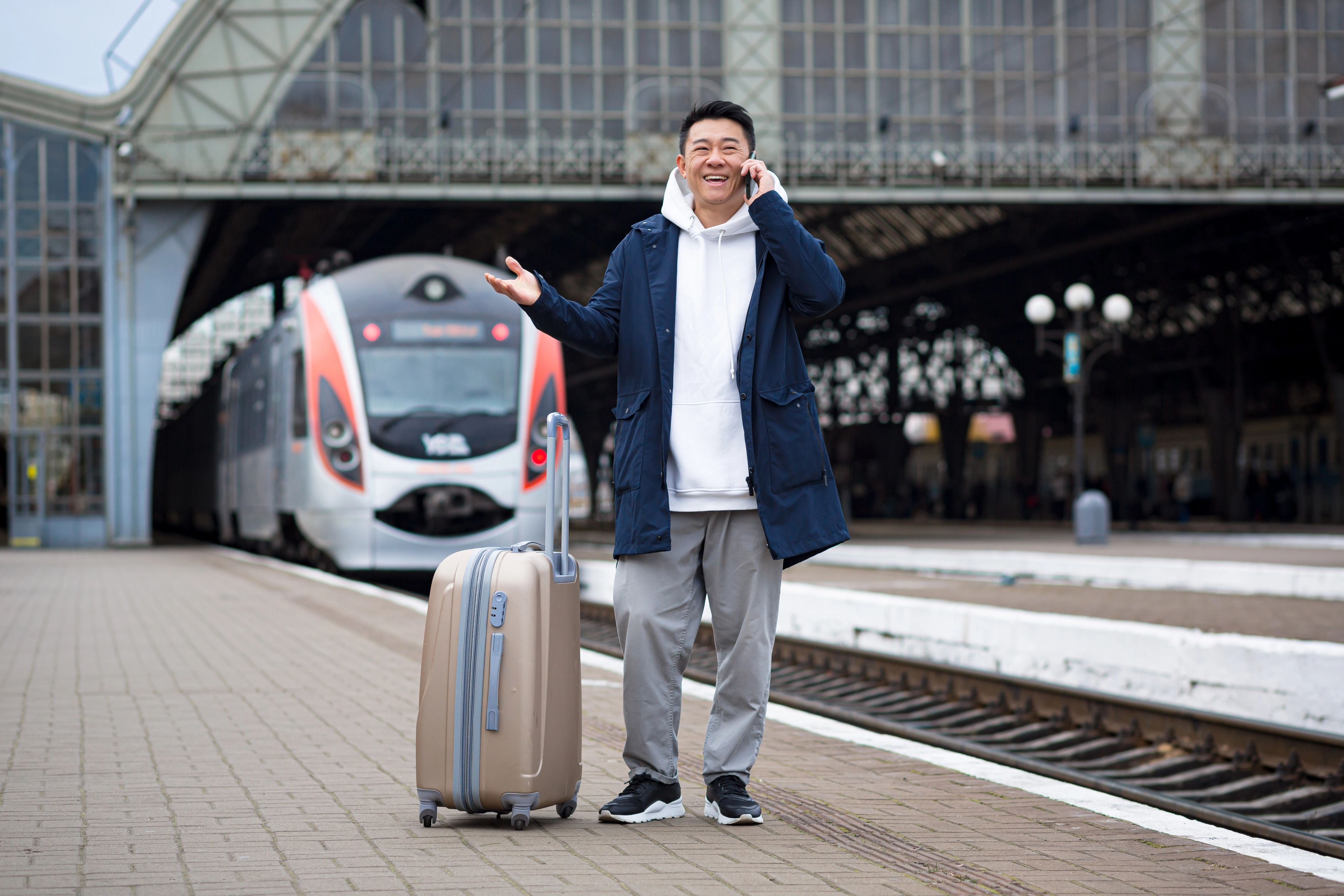 An image of a man of asian ethnicity talking on the phone walking in a train station