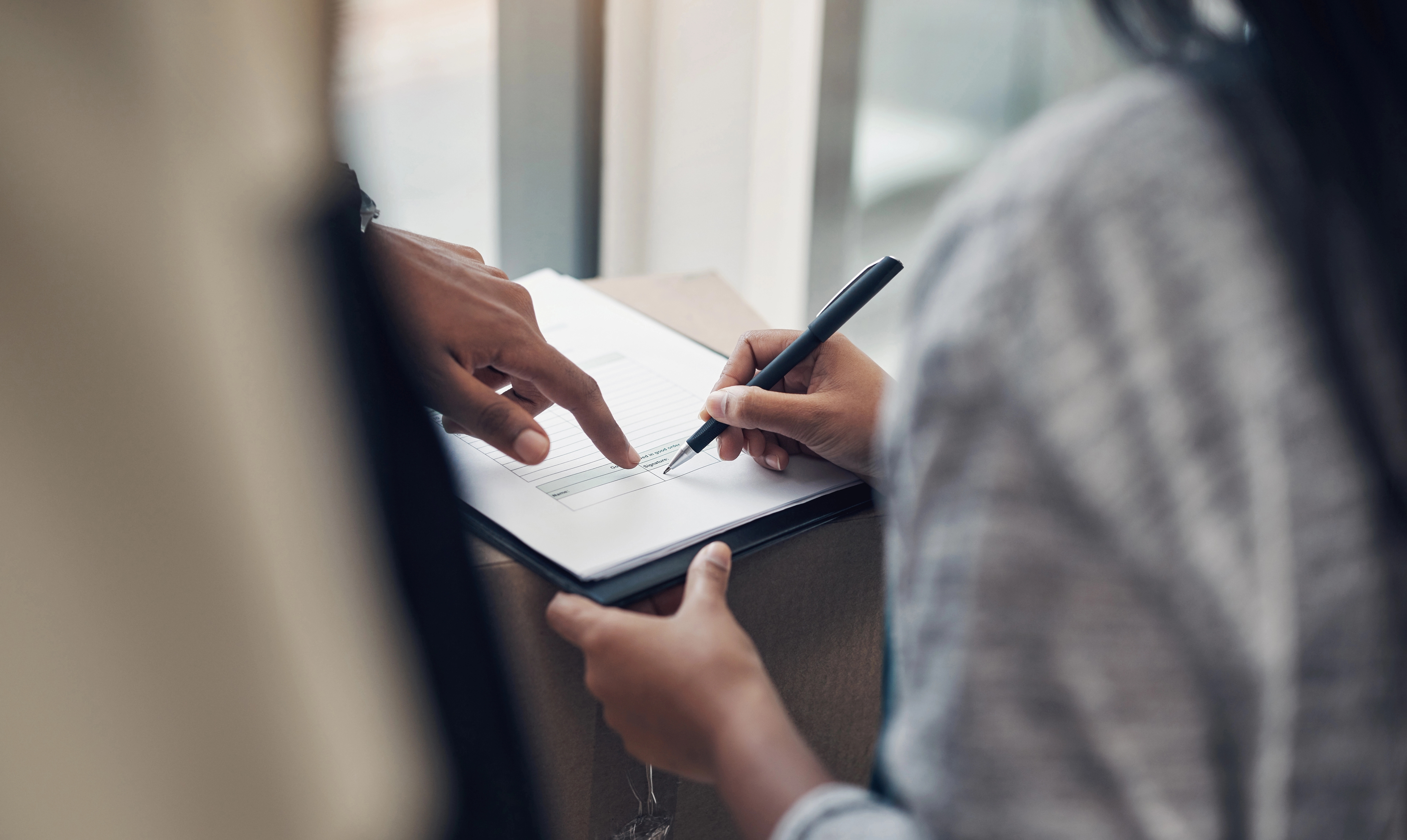 An image of a woman signing a contract with a male finger pointing at a line of text