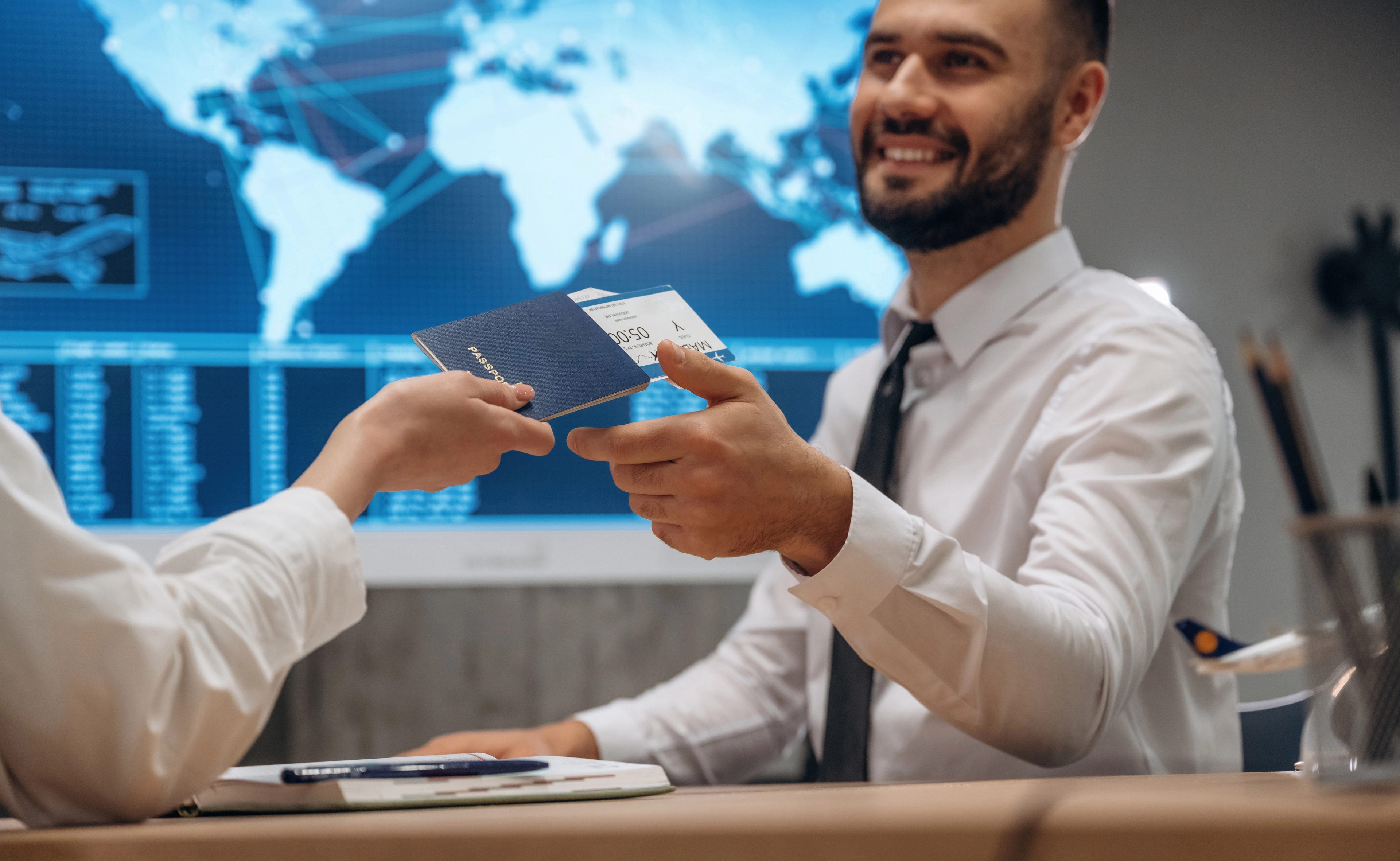 An image of an immigration officer taking a passport sitting infront of a world map