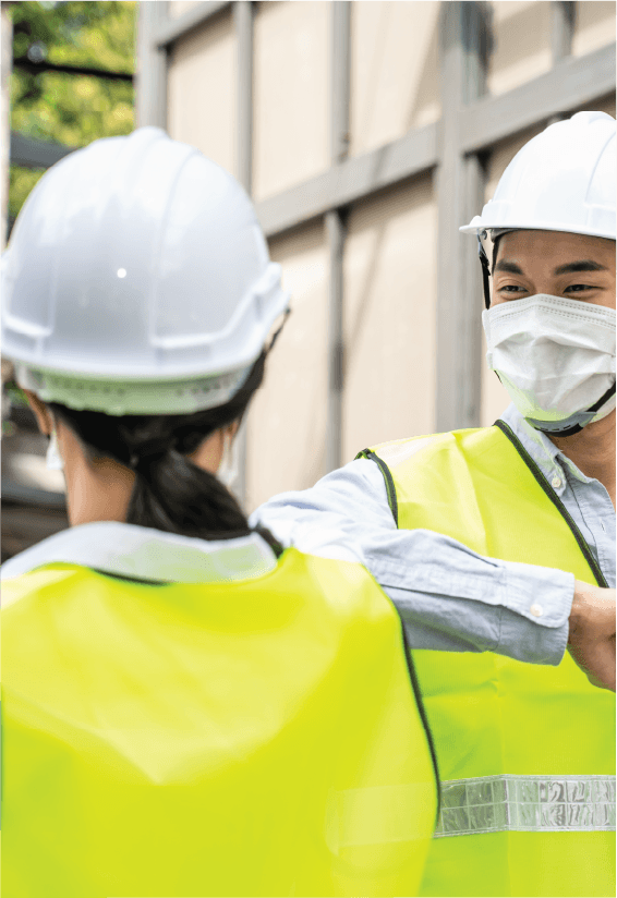 An image of two asian workers in safety uniforms greeting one another