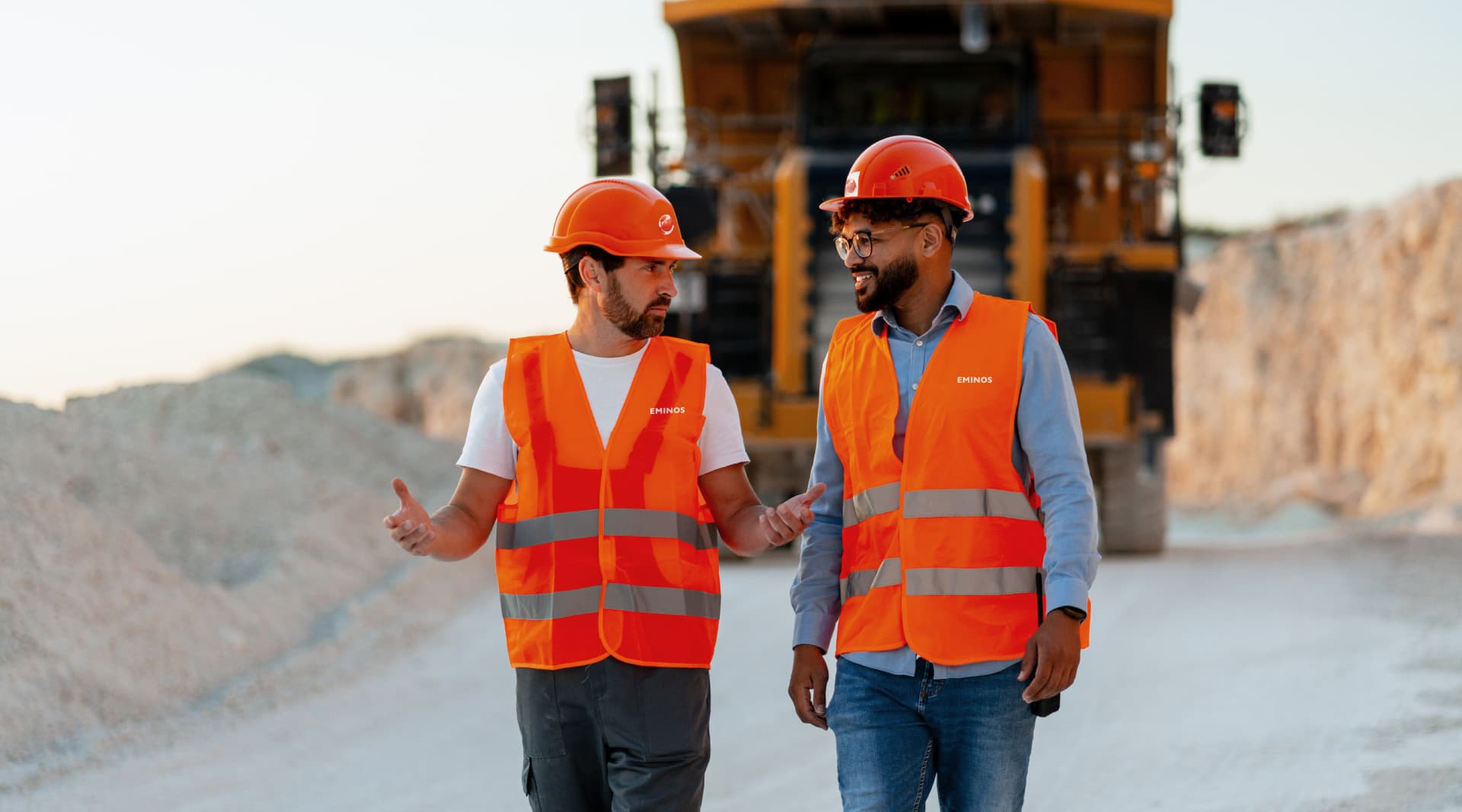 Two Eminos workers in safety gear talking on a mine site.